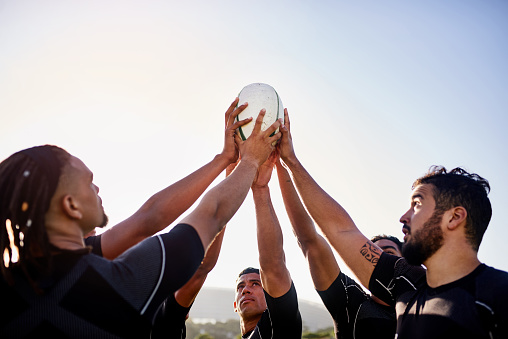 Cropped shot of a handsome group of sportsmen holding a rugby ball together before playing rugby