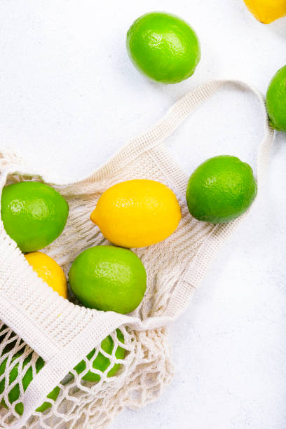 istock Organic lemons and limes in reusable eco-friendly string mesh bag. Zero waste, plastic free and sustainable lifestyle concept. White kitchen table background, copy space, top view 1222830229