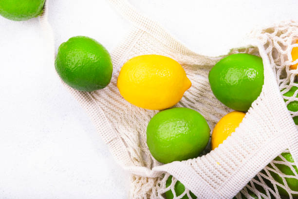 istock Organic lemons and limes in reusable eco-friendly string mesh bag. Zero waste, plastic free and sustainable lifestyle concept. White kitchen table background, copy space, top view 1222830286