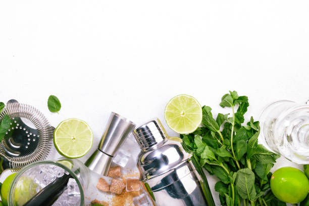 istock Mojito cocktail alcohol long drink making. Mint, lime, ice, white rum, cane sugar ingredients and bar utensils. Top view, white table background. Flat lay 1222831342