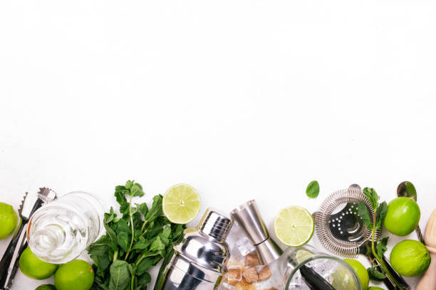 istock Mojito cocktail alcohol long drink making. Mint, lime, ice, white rum, cane sugar ingredients and bar utensils. Top view, white table background. Flat lay 1222831377