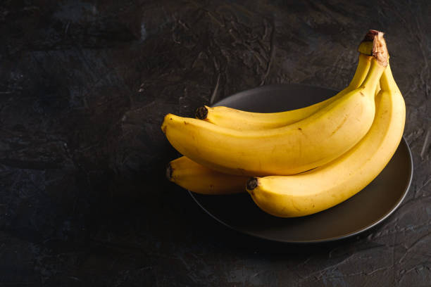 istock Banana fruits in black plate on dark textured background, angle view copy space 1222838025