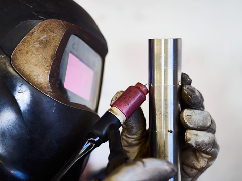 Welder tack welding a stainless pipe, wearing protective helmet and gloves.