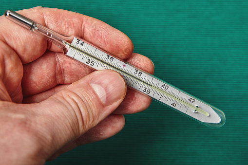 A glass mercury thermometer shows the high temperature of a person’s body on its scale.
