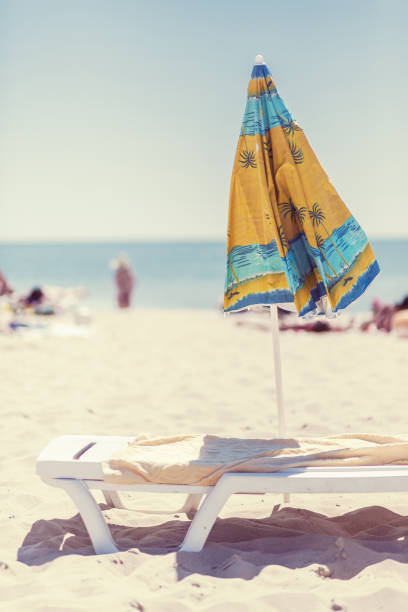 istock Summer vertical composition of a beach umbrella and deck chair with a carelessly thrown beach towel. Sun sand sea and beach 1222844246