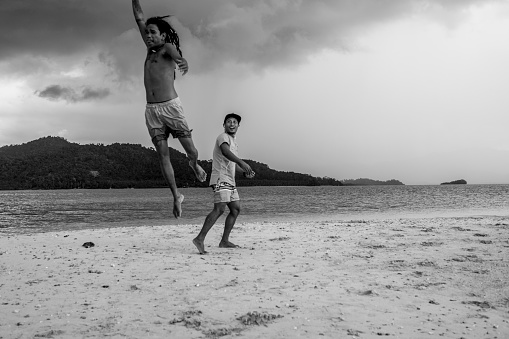 Two Filipino men enjoy a few minutes of fun on a small sandbar in the middle of the sea near Port Barton, Palawan. One man is jumping high into the air.