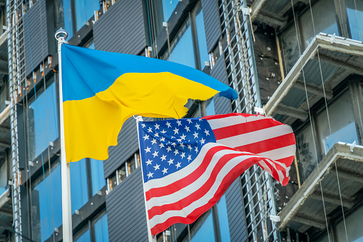 Banderas estadounidenses y ucranianas ondean contra el cielo azul y parte del edificio. Patriotismo. photo