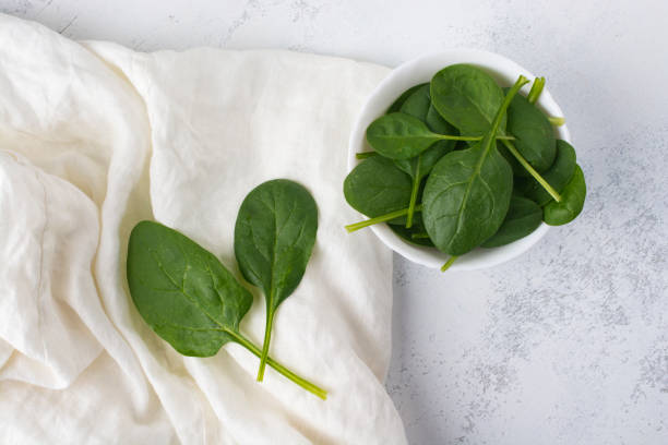 istock Green spinach leaves in a white bowl on a white table. View from above. 1222845486