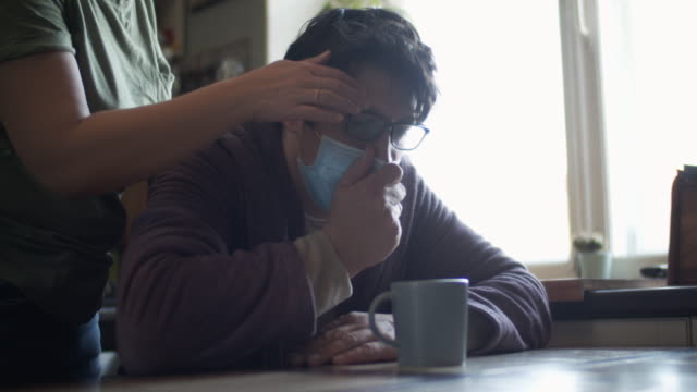 Woman taking care of her sick husband wearing protective mask and coughing