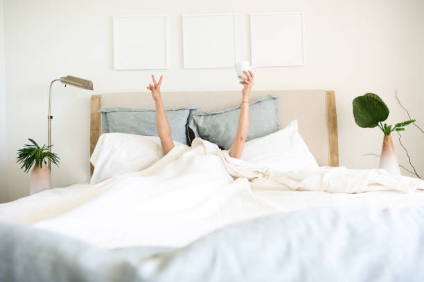 hispanic mature woman waking up in bed with coffee mug in hand - headboard imagens e fotografias de stock