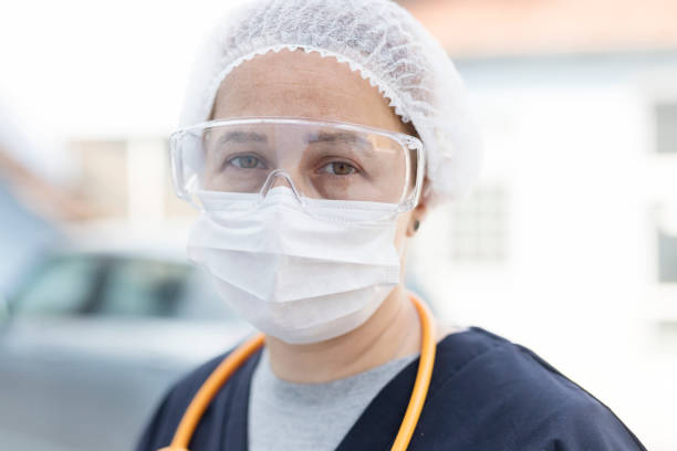 Head shot of young woman with protective mask, glasses and stethoscope in a medical outfit stock photo