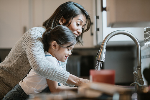 A mom teaches her little girl how to properly wash and disinfect her hands to keep them free of virus and bacteria germs.  Part of a regular routine, or the new normal with social distancing and working from home during the Covid-19 Pandemic.