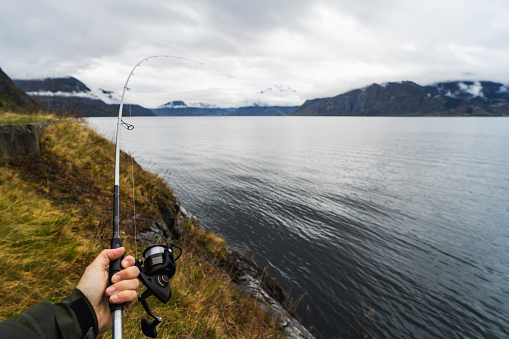POV man fishing with a rod in the sea by a fjord, in Norway