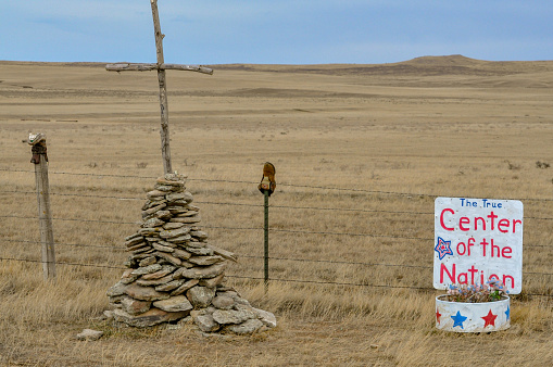 Wooden cross held up with pile of rocks by a red, white, and blue sign saying \