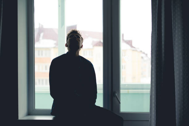 istock sad lonely thoughtful man silhouette sitting on a window windowsill and looking outdoors far away, 1222865504