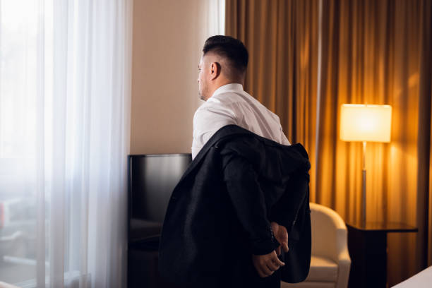 ホテルの部屋でジャケットを脱ぐ若い男、後ろ見 - undressing ストックフォトと画像