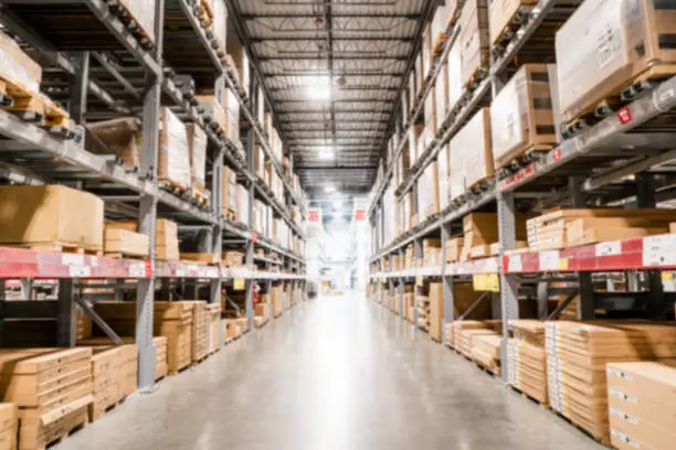 Photo of Blurred view of the interior of a warehouse; boxes stacked up high on both sides of an aisle