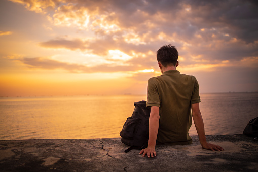 Rear view of teenage traveler looking at sunset at seaside