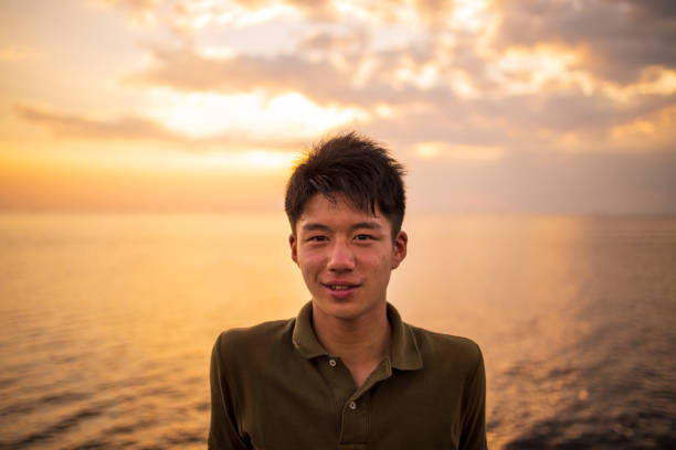 Portrait of teenage traveler sitting near sea at sunset time stock photo