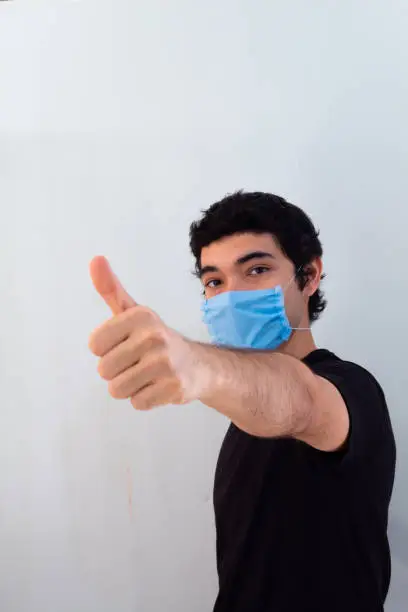 young man wearing a blue medical mask on a white background gesturing with his hands that everything will be fine