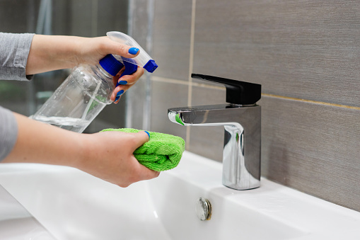 Side view on female hands holding cloth and spray sanitizer disinfection alcohol in hand cleaning sink tap faucet in bathroom to disinfect from virus or bacteria and clean limescale prevent infection