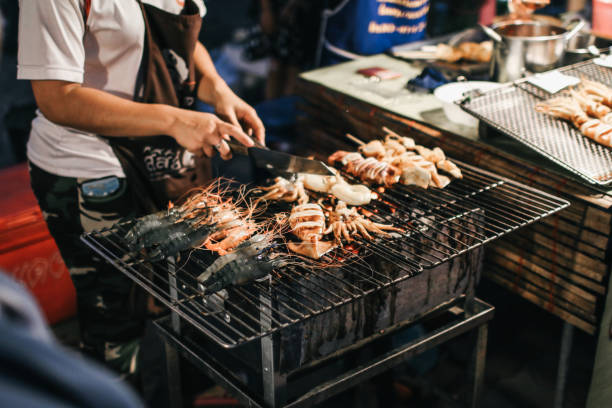 chef cozinhar delicioso churrasco de cozinha asiática grelhado lula fresca em um fogão a carvão para venda no mercado local. festa de frutos do mar assados mercado noturno de comida de rua tailandês. lula e polvo grelhados. - adulation asia cooked food - fotografias e filmes do acervo