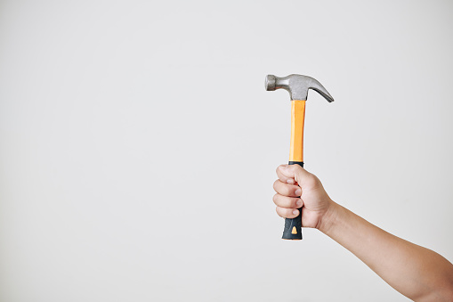 Hand of repairman holding hammer against black light grey wall