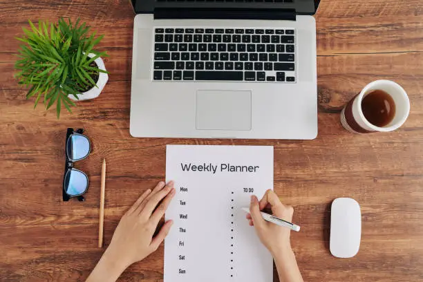 Woman writing weekly planner to stay productive when working from home during quarantine period