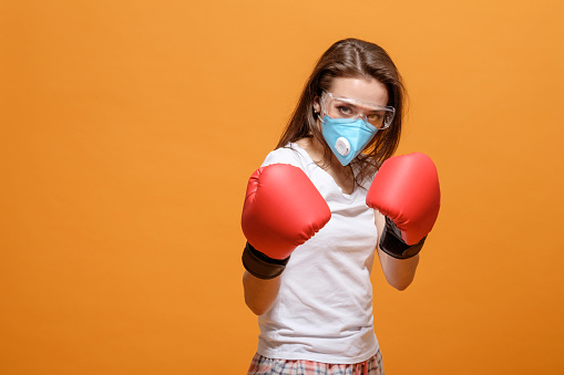 woman in boxing gloves, home quarantine, coronavirus pandemic, on yellow orange background, battle fight with virus
