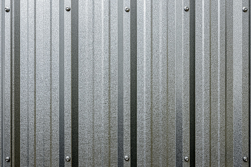 Reflective, abstract, corrugated, galvanized, zinc metal, roofing sheet as a modern architectural feature background showing the character of the ridge profiles with fastener bolts securing the roof metal sheeting, seen at the top and the bottom of the image framing the center making good copy space in the center. Good, clean, modern architectural abstract background with good copy space.
