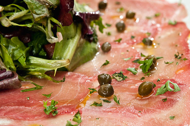 Gourmet beef carpaccio rolls filled with arugula and topped with parmesan shavings, served on a fine dining plate with a painted sauce.