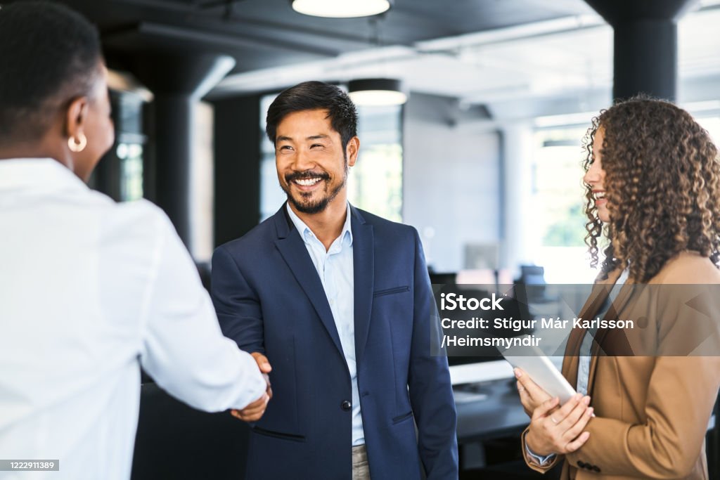 Smiling businessman shaking hands with colleague Smiling businessman shaking hands with female professional. Young businesswoman is holding digital tablet. They are standing at office. Handshake Stock Photo