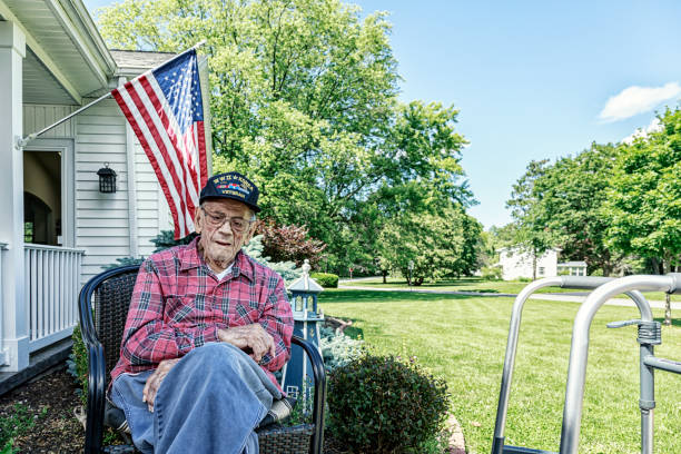 WWII and Korean Conflict USA Military Veteran At Home Authentic, 96 year old, senior adult, real person, real life, WWII and Korean War USA military veteran patriot sitting outside his home near Rochester in western New York State on a sunny June summer day. He's become quite frail, so he keeps his medical mobility walker close by to support himself walking when he decides to go back inside. He is wearing a generic souvenir military veteran's service baseball cap style hat - a symbol commemorating his World War II US Army, and Korean War US Air Force military service. us military photos stock pictures, royalty-free photos & images