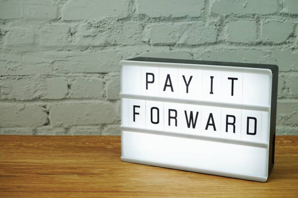 istock Pay It Forward word in light box with space copy on white brick wall and wooden background 1222917167
