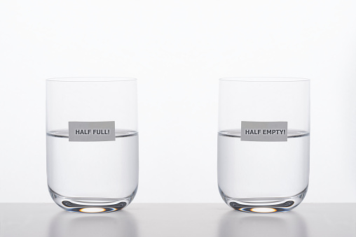 Two drinking glasses with water on white background. Half full is written on one glass and half empty on the other glass. Representing different  point of views about the same facts.