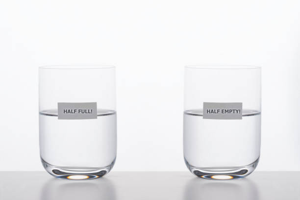 Half Full and Half Empty Two drinking glasses with water on white background. Half full is written on one glass and half empty on the other glass. Representing different  point of views about the same facts. half full stock pictures, royalty-free photos & images