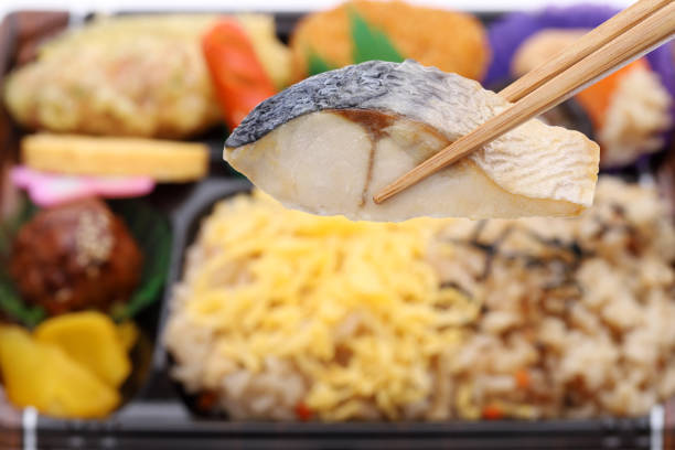 Japanese bento lunch background, grilled fish held with chopstick, close up