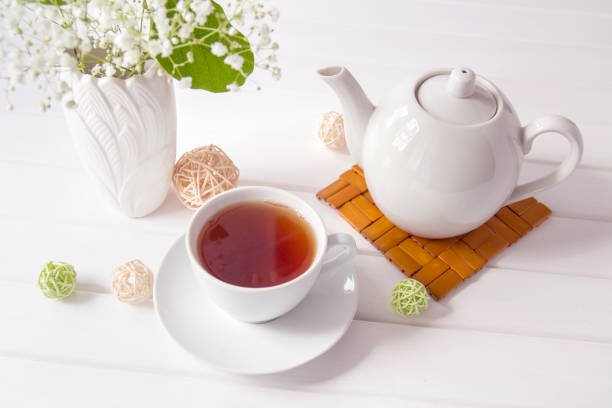 istock White ceramic cup and tea pot, vase with flowers on white wooden table background. Beautiful setting the table for Breakfast and tea time. The concept of Beginning of the day good morning 1222929350