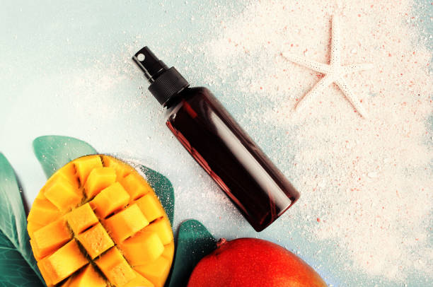 Cosmetic product in spray bottle top view summer skin care background, mango fruit, beach sand, pastel toned. Summertime beauty treatment, safe, natural, and aromatic perfume sprayer photos stock pictures, royalty-free photos & images