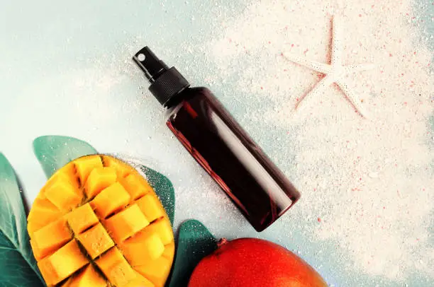 Photo of Cosmetic product in spray bottle top view summer skin care background, mango fruit, beach sand, pastel toned.