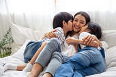 Happiness of Asian family with mom and son and daughter hug and kissing mother on white bed in bedroom, Feeling happy and family relationship concept