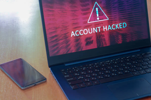 istock Hacked account concept on laptop screen and cellphone on a table with a dark screen. Warning triangular sign with exclamation mark symbol. Red abstract background. Horizontal. 1222934232