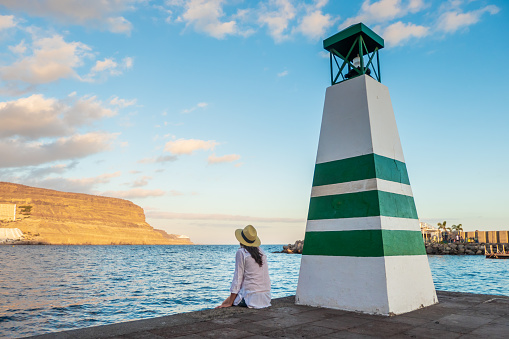 Young woman \nlooking at the sea by the lighthouse in puerto de mogan, Gran Canaria, canary islands, Spain.