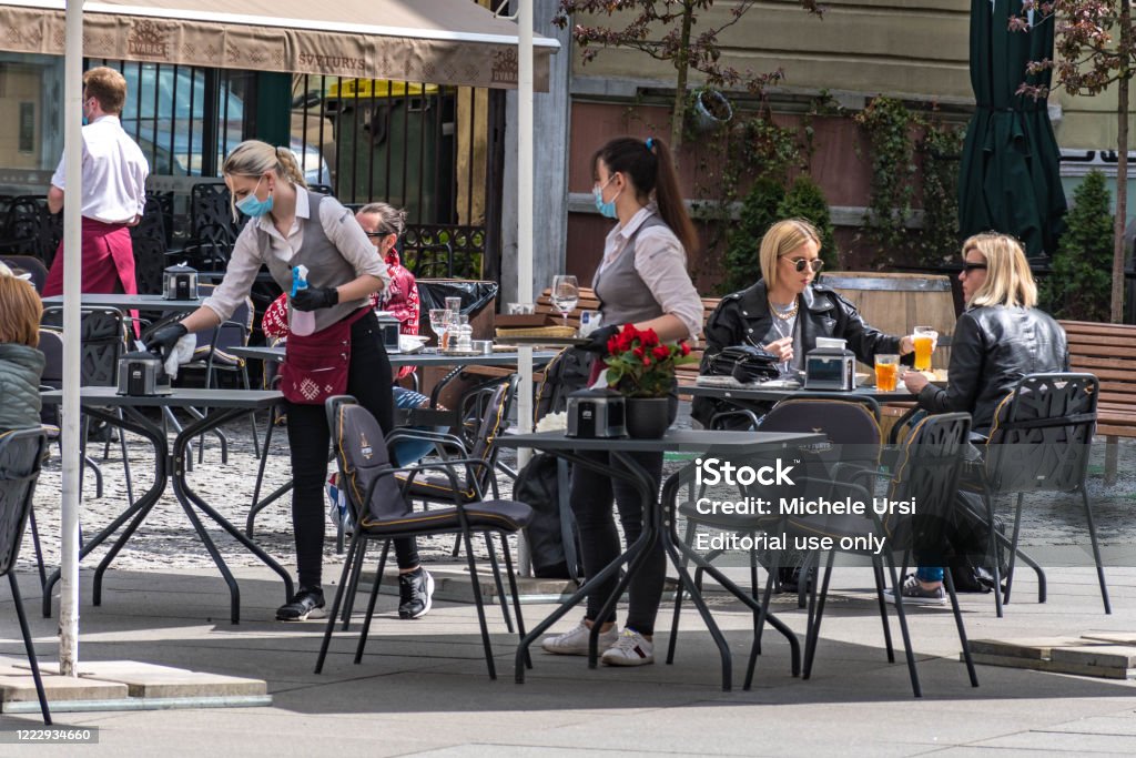 Camareras con una máscara y guantes desinfectando la mesa de un bar, cafetería o restaurante al aire libre - Foto de stock de Restaurante libre de derechos