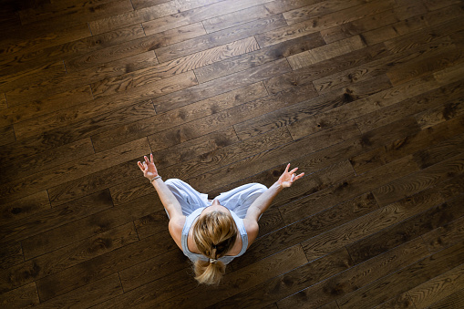 High angle view of a woman doing Yoga exercises in Lotus position on parquet floor at home. Copy space.