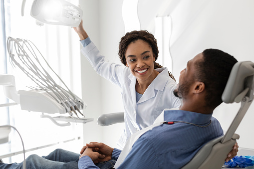 Beautiful black woman dentist greeting male patient on her workplace, copy space