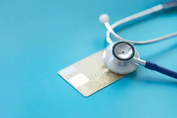 Stethoscope on Mock up Credit Card with number on cardholder in hospital desk. Health insurance and cost of care, self-care during illness using payments card for medicals service.