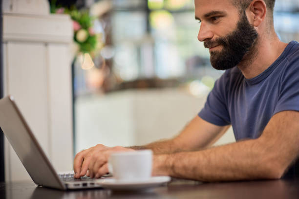 istock Young bearded Caucasian man sitting in restaurant and using laptop. 1222940918