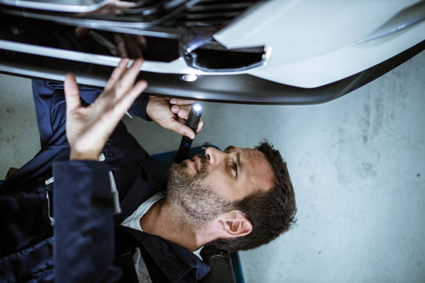 Above view of auto mechanic analyzing the chassis problem. High angle view of young car mechanic analyzing undercarriage of a car with a lamp. car mechanic top view stock pictures, royalty-free photos & images