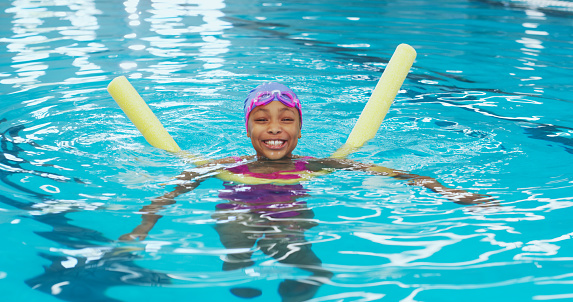 Portrait of an adorable young girl using a pool noodle during a swimming lesson